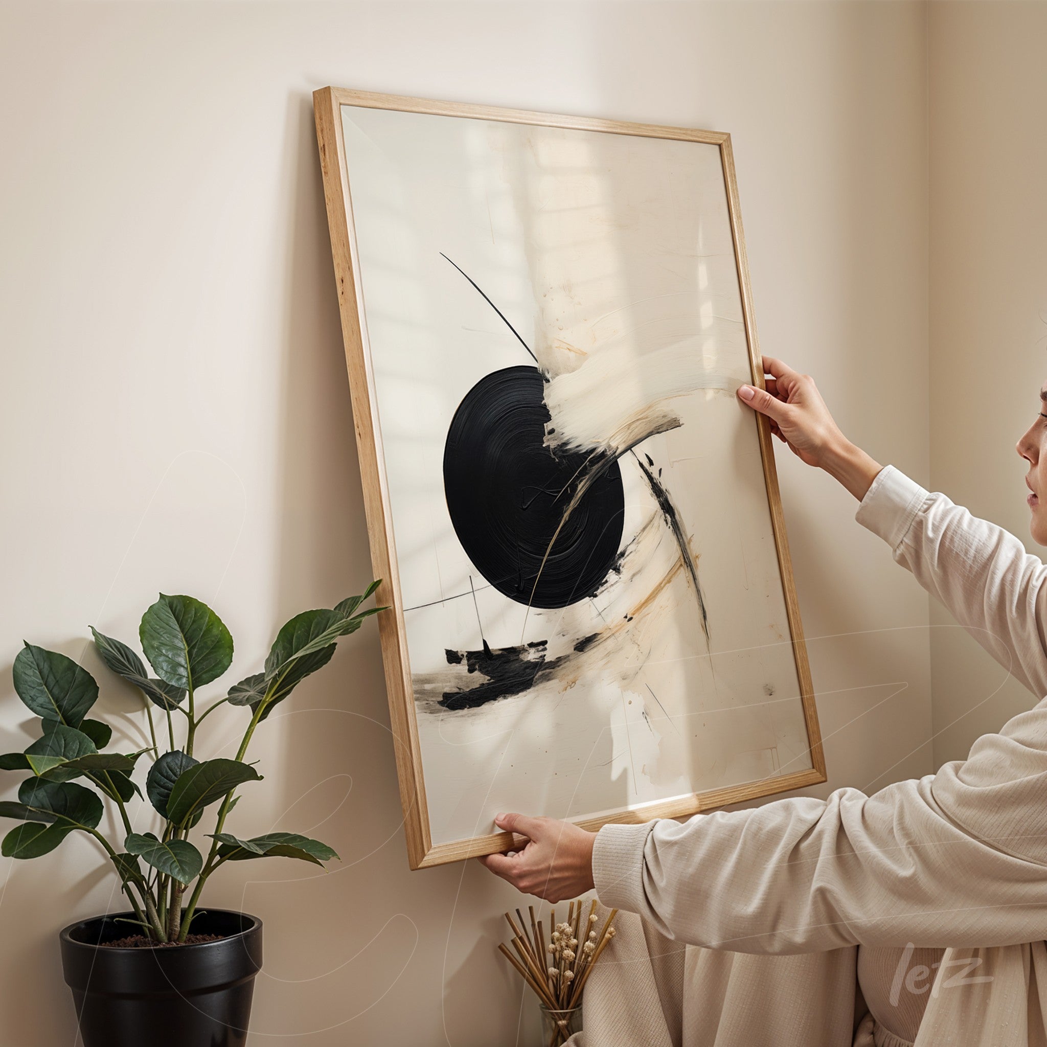 quadro com arte abstrata em moldura de madeira clara, apresentado em ambiente minimalista com planta em vaso ao lado