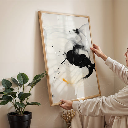 quadro com arte abstrata em preto e branco em moldura de madeira clara, sendo segurado por uma pessoa em ambiente aconchegante