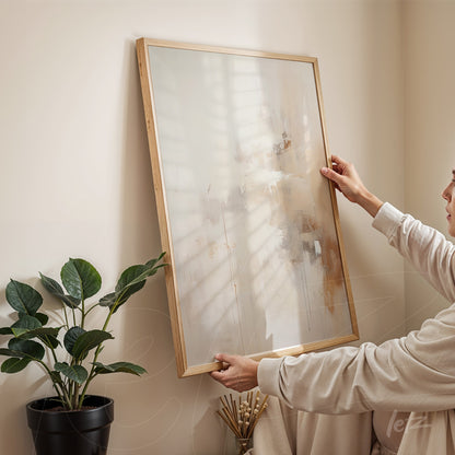 quadro abstrato em moldura de madeira clara, sendo segurado por pessoa em ambiente iluminado