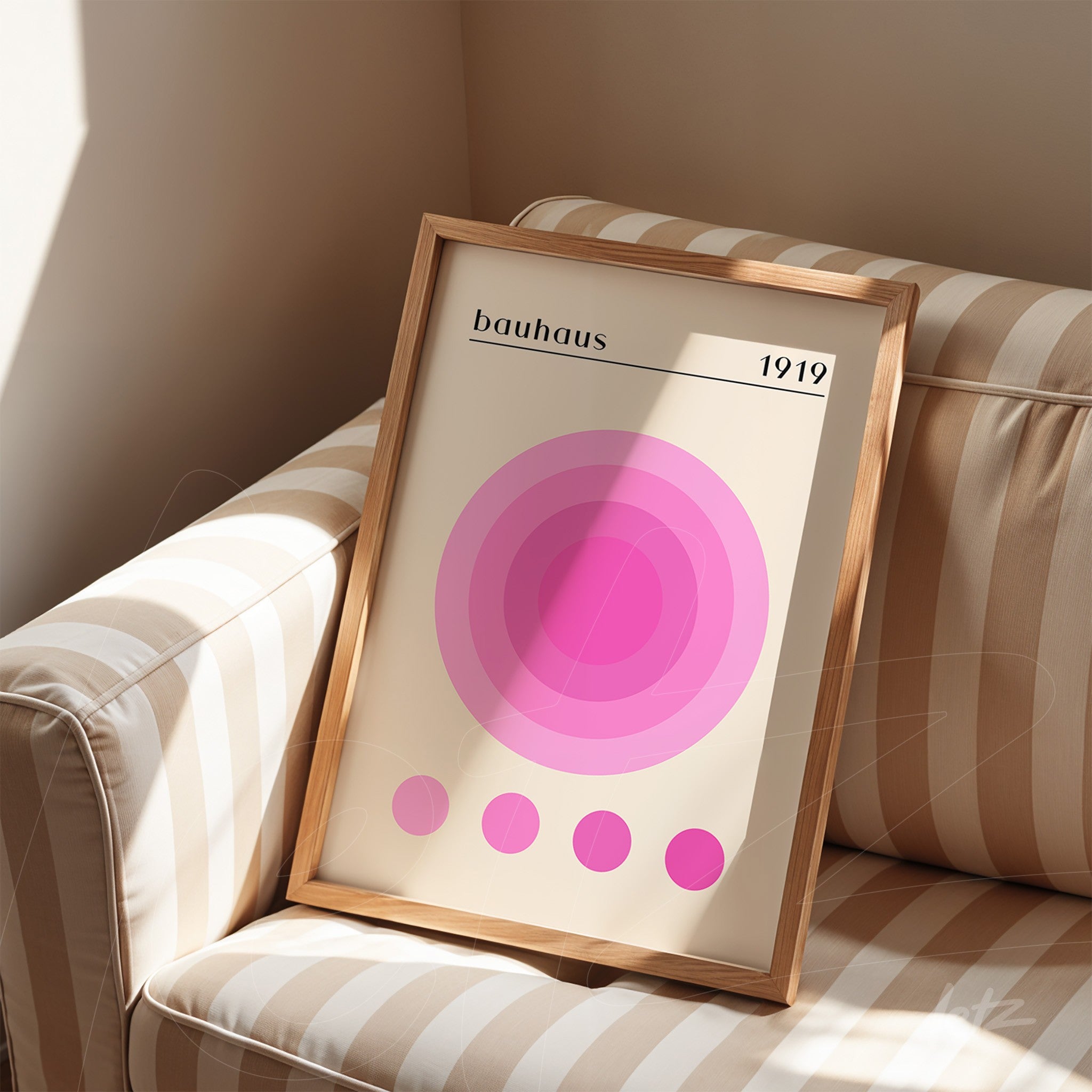 pôster impresso de círculos concêntricos rosa em tons variados com texto 'bauhaus 1919' exibido em moldura de madeira sobre sofá listrado
