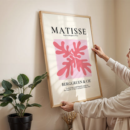 quadro com arte moderna em moldura de madeira clara, com fundo rosa e formas orgânicas em tons de vermelho e rosa