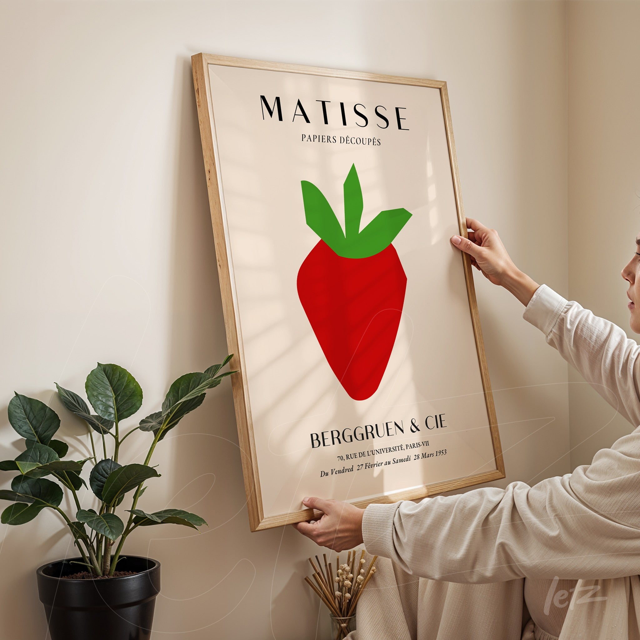 quadro com arte moderna de uma maçã vermelha em fundo claro, moldura de madeira natural, pessoa ajustando o quadro na parede