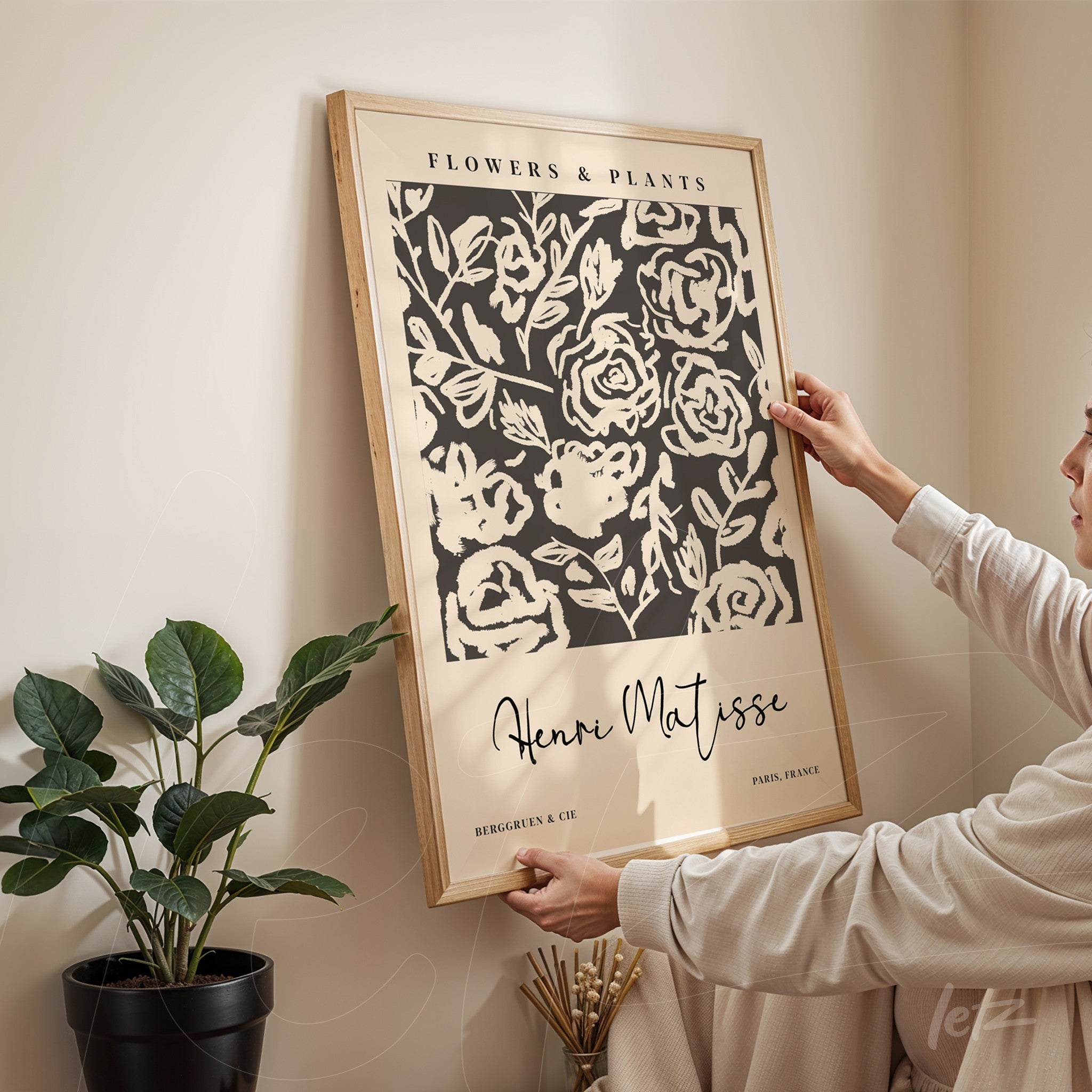 quadro decorativo com flores estilizadas em fundo preto e moldura de madeira clara, sendo segurado por uma pessoa em ambiente interno