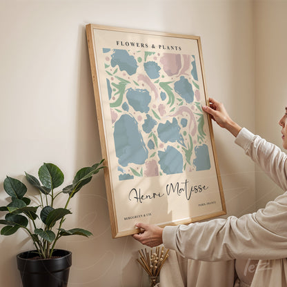 quadro decorativo com arte abstrata em tons pastel de flores e plantas, moldura de madeira clara, parafusado na parede, com uma mulher em destaque segurando o quadro