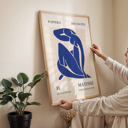 quadro com arte moderna de figura feminina em tons de azul em moldura de madeira clara, apoiado em parede beige