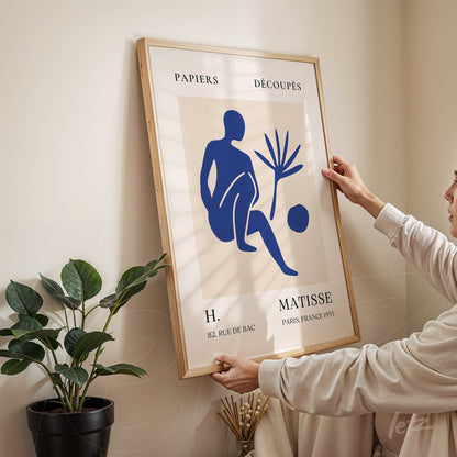 quadro com arte de figura estilizada em azul sobre fundo claro, moldura de madeira clara