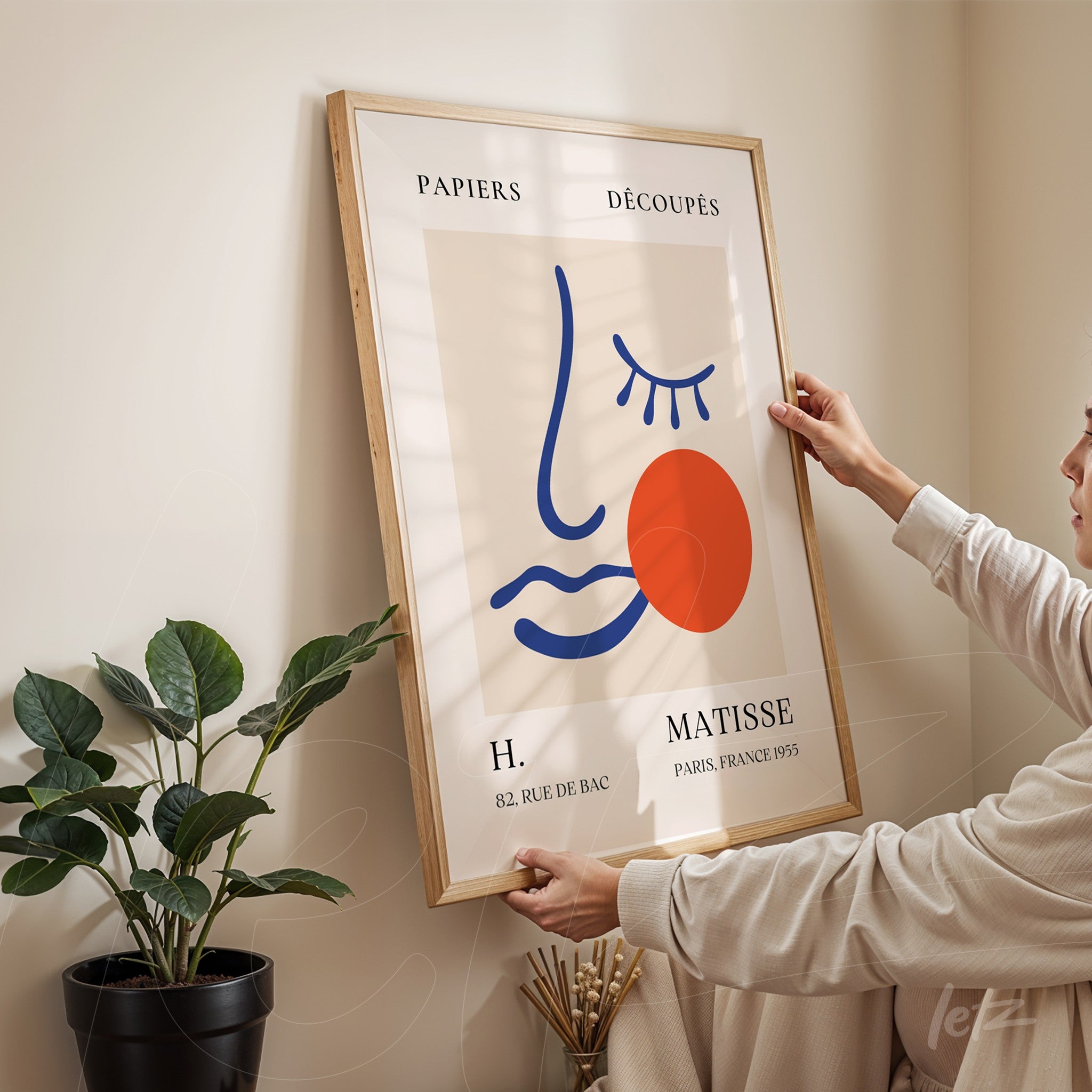 quadro em moldura de madeira clara com arte moderna de rosto, fundo claro e detalhes em cores primárias, exposto em parede neutra