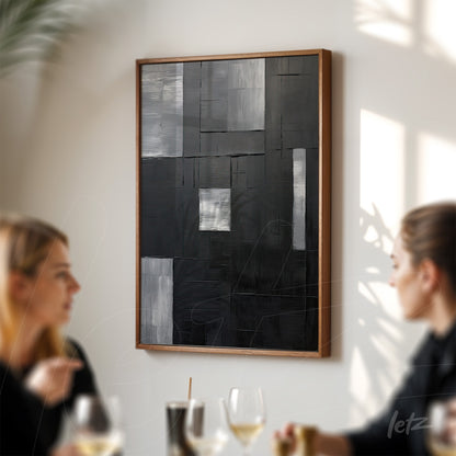 quadro abstrato em preto e branco com texturas em uma moldura de madeira clara, exibido em parede iluminada ao fundo de um ambiente com pessoas