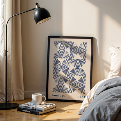 quadro com arte geométrica em estilo bauhaus apoiado no chão ao lado de cama, com moldura preta