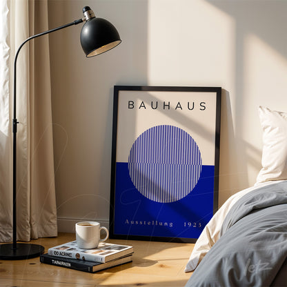 quadro com arte geométrica moderna estilo Bauhaus em moldura preta, apoiado no chão ao lado de cama e luminária