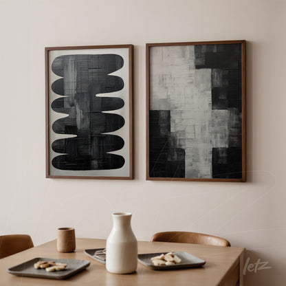 composição de dois quadros modernos em moldura de madeira, um com formas abstratas em preto sobre fundo branco e o outro em tons de cinza e preto, exibidos sobre parede clara em ambiente minimalista