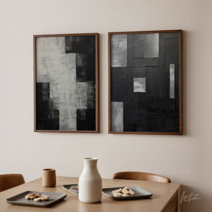 composição com dois quadros abstratos em tons de preto e cinza, em moldura de madeira clara, expostos em parede neutra acima de mesa de madeira clara