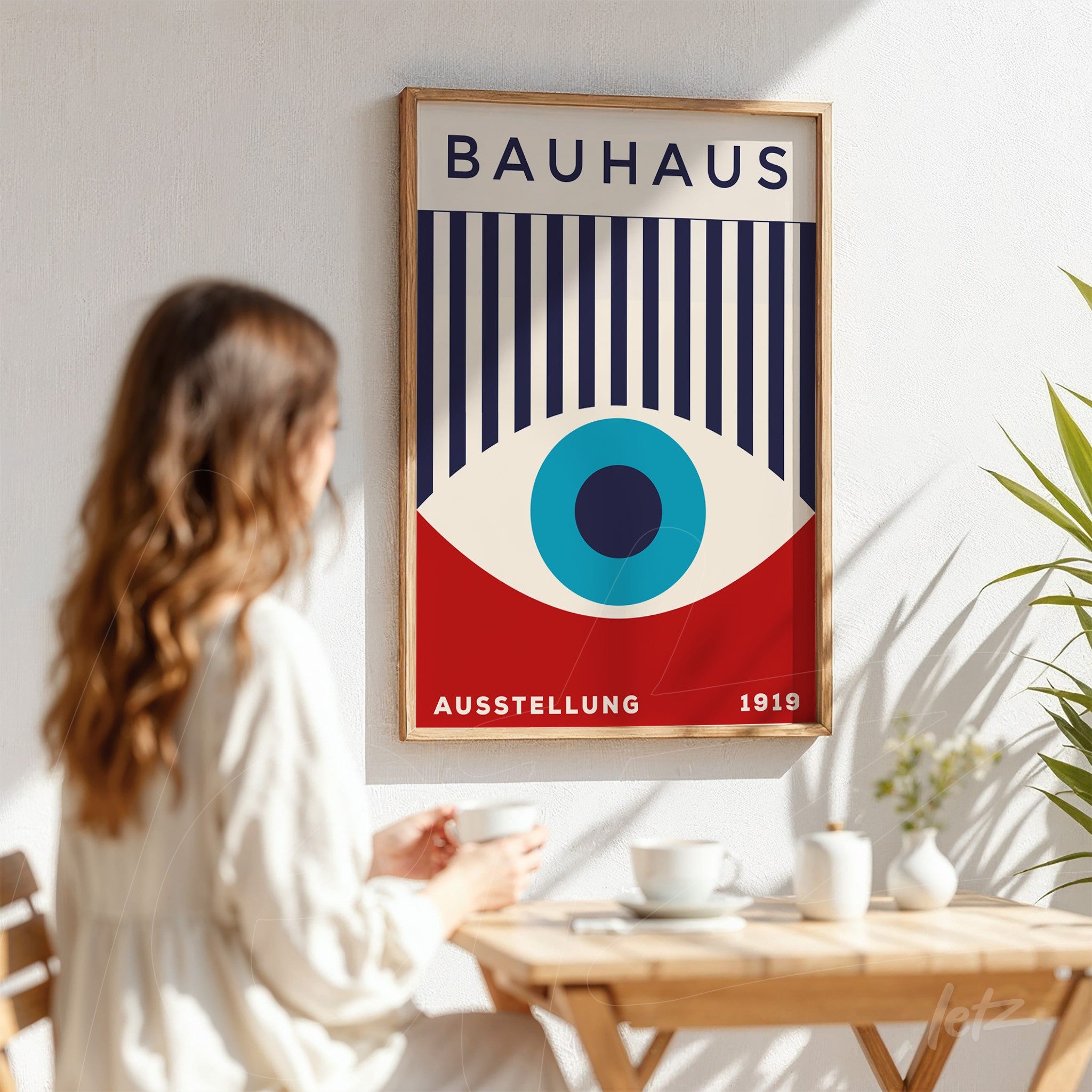 pôster impresso com arte em estilo Bauhaus de um olho azul centralizado, listras verticais e moldura de madeira clara, exibido em parede branca ao lado de mulher sentada