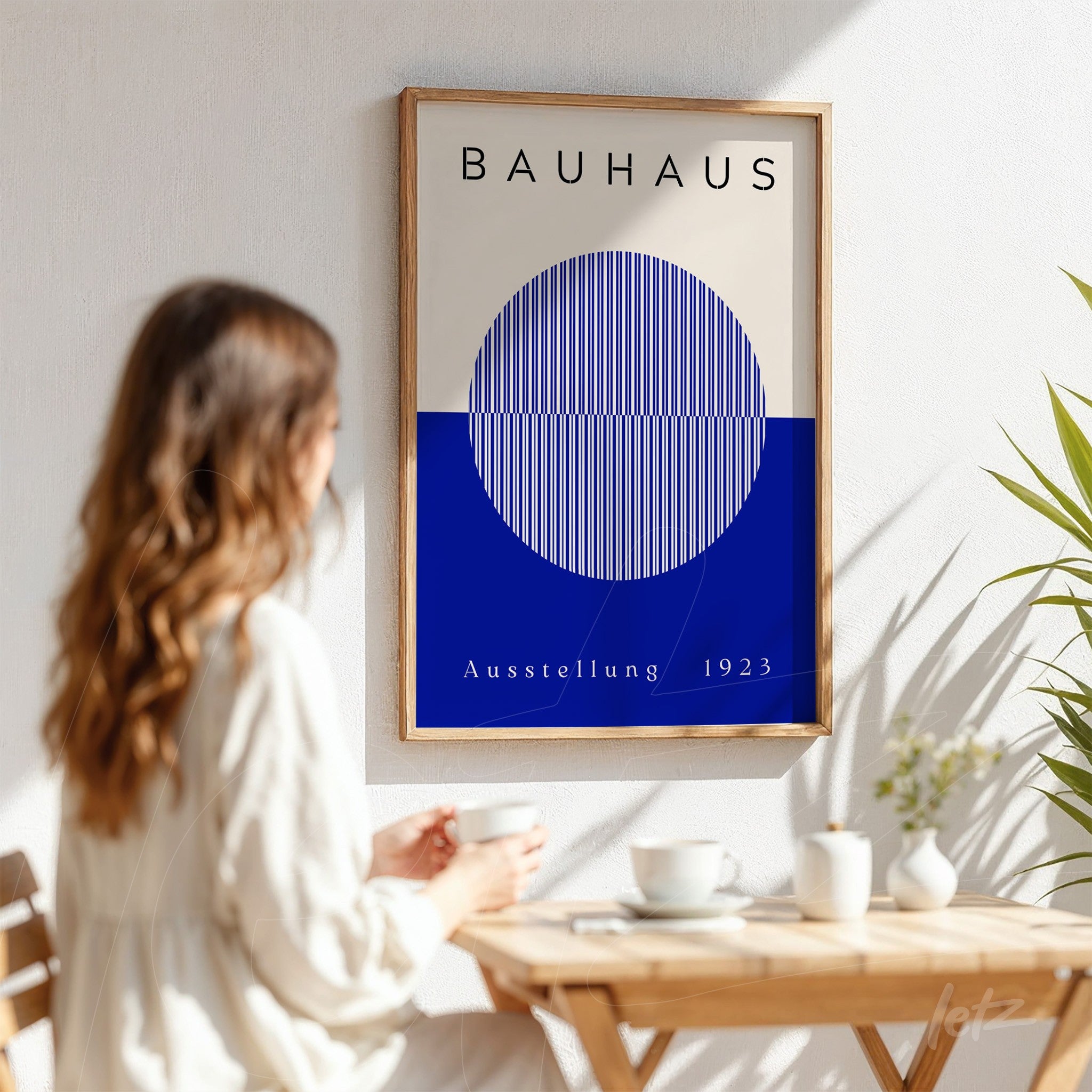 pôster com design geométrico em estilo Bauhaus com círculo azul e listras em fundo bege, exibido em moldura de madeira clara sobre parede branca
