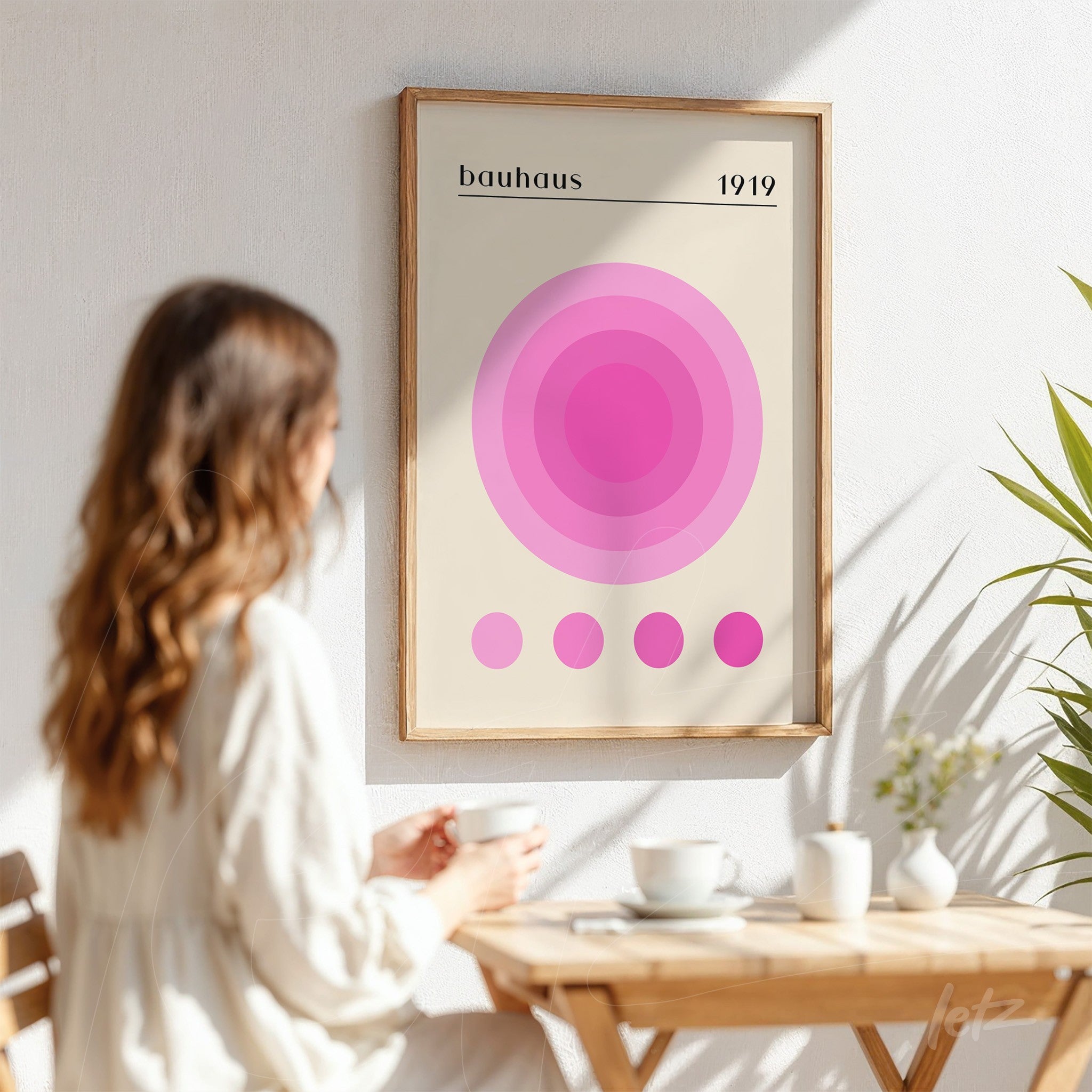 quadro com design geométrico em círculos rosa inspirado no estilo Bauhaus, emoldurado e exibido em parede branca ao lado de planta
