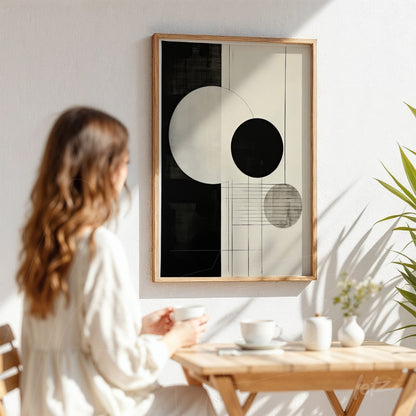 quadro com arte abstrata em preto e branco em moldura de madeira clara exibido em parede branca, com círculo grande e círculos menores em composição geométrica
