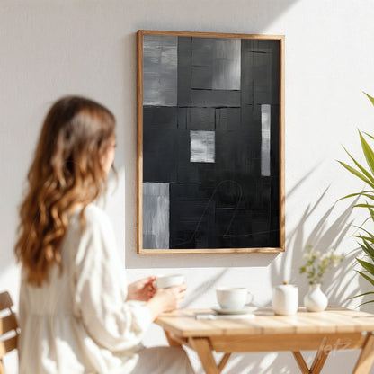 quadro abstrato em tons de preto e cinza com acabamento em moldura de madeira clara, exibido sobre parede branca