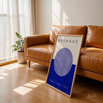quadro decorativo estilo Bauhaus com moldura de madeira clara exibido apoiado em sofá de couro marrom em ambiente bem iluminado