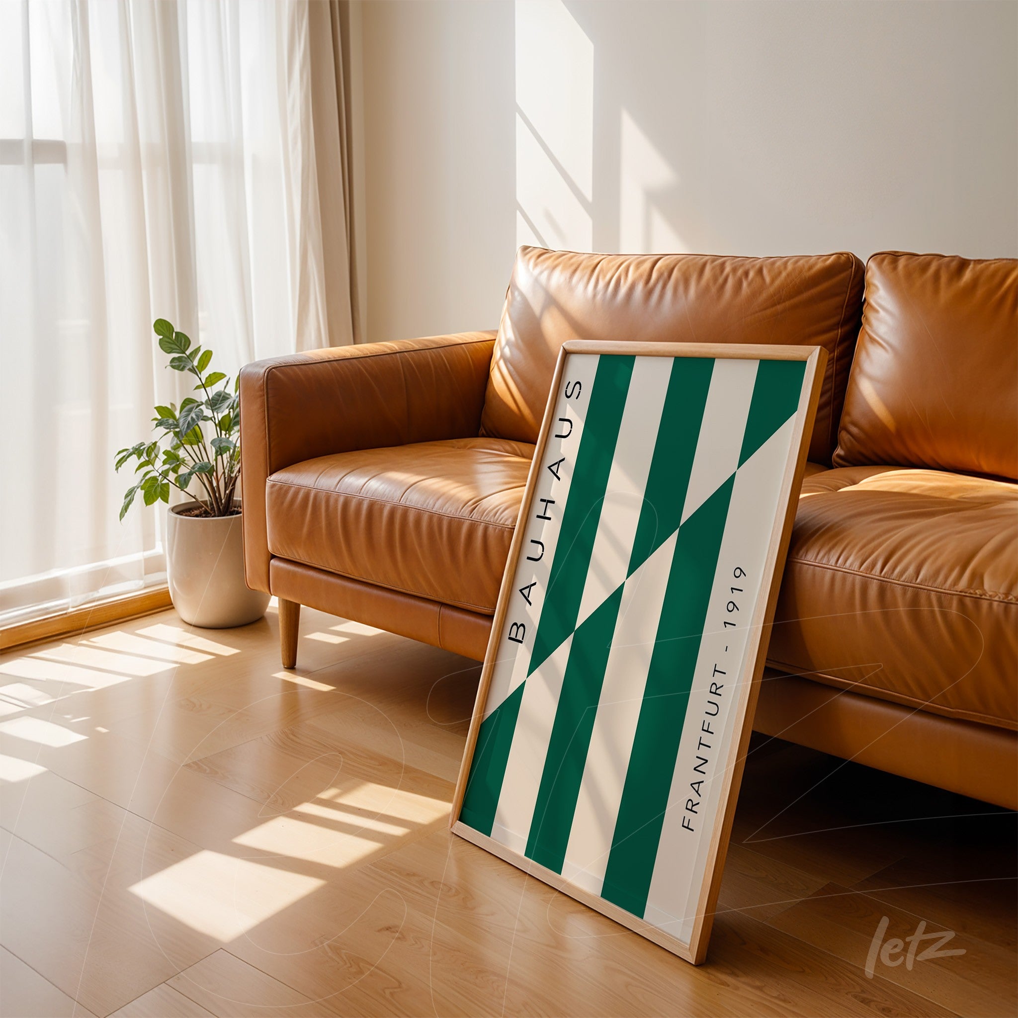 quadro com design geométrico verde e branco, escrito bauhaus em moldura clara, apoiado em sofá de couro marrom