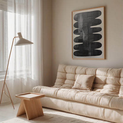 quadro abstrato em moldura clara com formas ovais em tons de preto, exibido em sala de estar minimalista com sofá bege e mesa de madeira clara