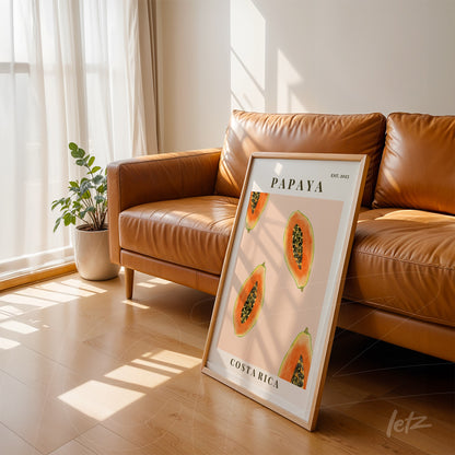 quadro com arte de papaias em moldura branca apoiado em sofá de couro caramelo com luz natural