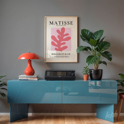 quadro com arte moderna de folha rosa em moldura clara exibido acima de móvel azul em ambiente decorado com plantas