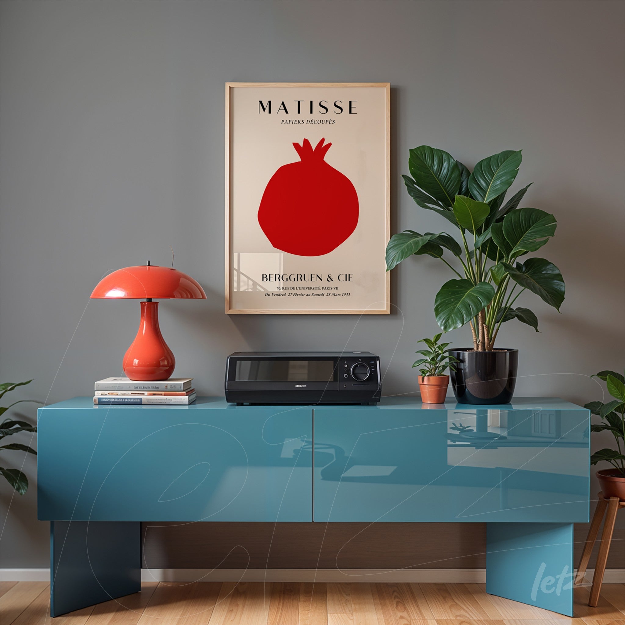 quadro emoldurado com arte do artista Matisse, apresentando uma romã vermelha em fundo claro, exposto sobre uma mesa azul brilhante com uma lâmpada laranja e uma planta em vaso