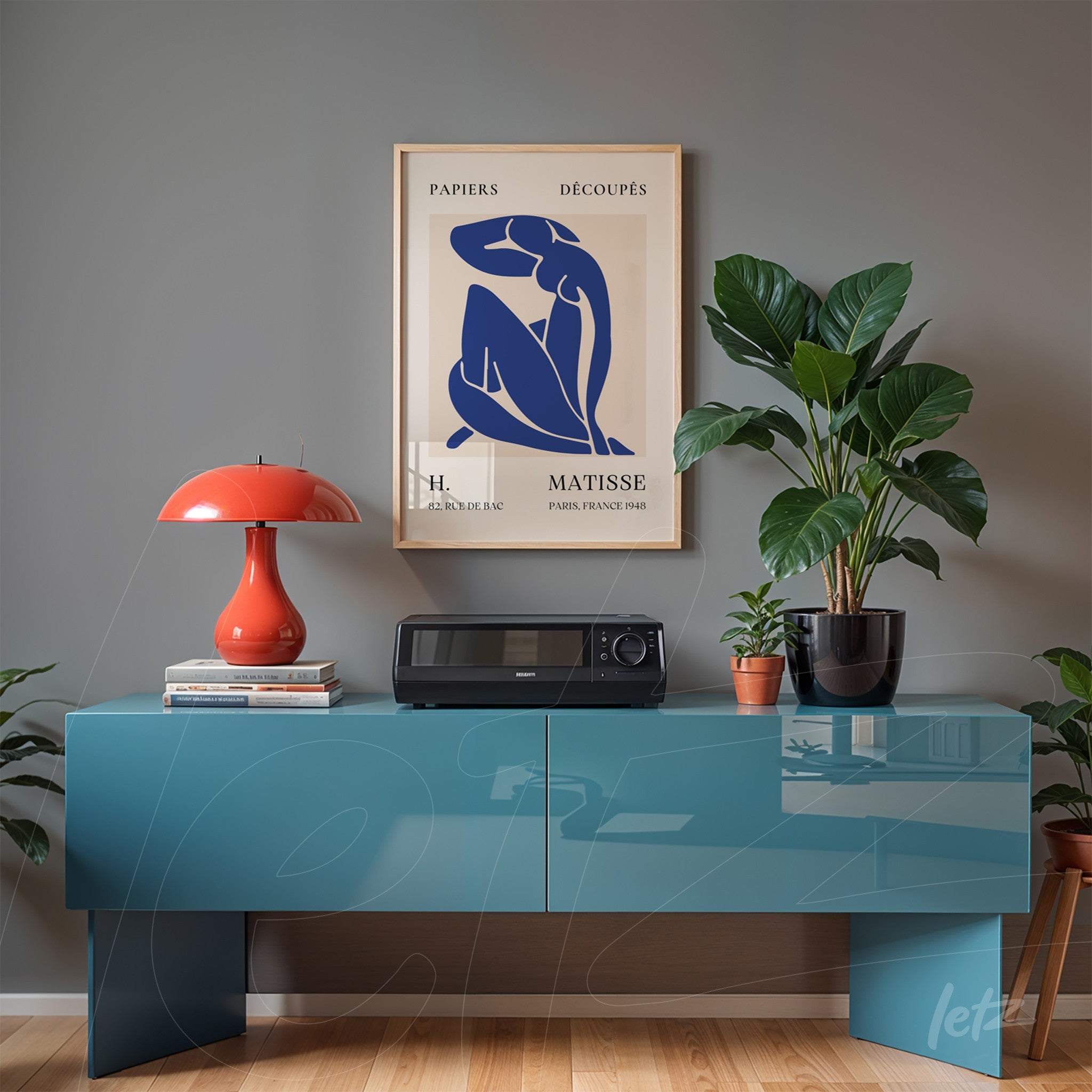 quadro com arte moderna de figura feminina em moldura clara, apoiado sobre móvel azul em ambiente com plantas