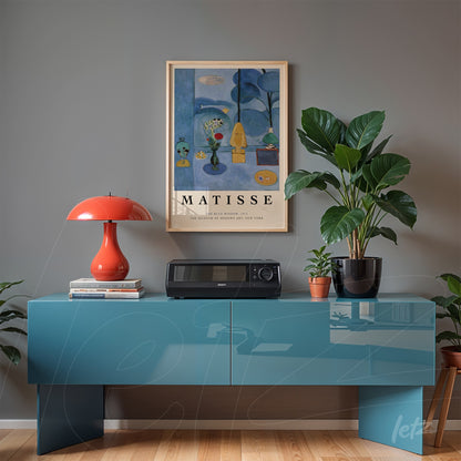 quadro emoldurado com arte de Henri Matisse sobre parede cinza, decorado com mesa azul e luminária vermelha