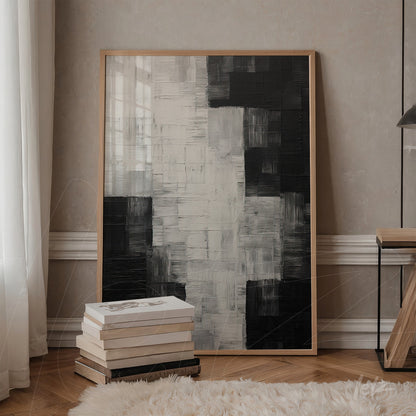 quadro abstrato em tons de preto e branco com moldura de madeira clara, apoiado em mesa de madeira ao lado de livros empilhados