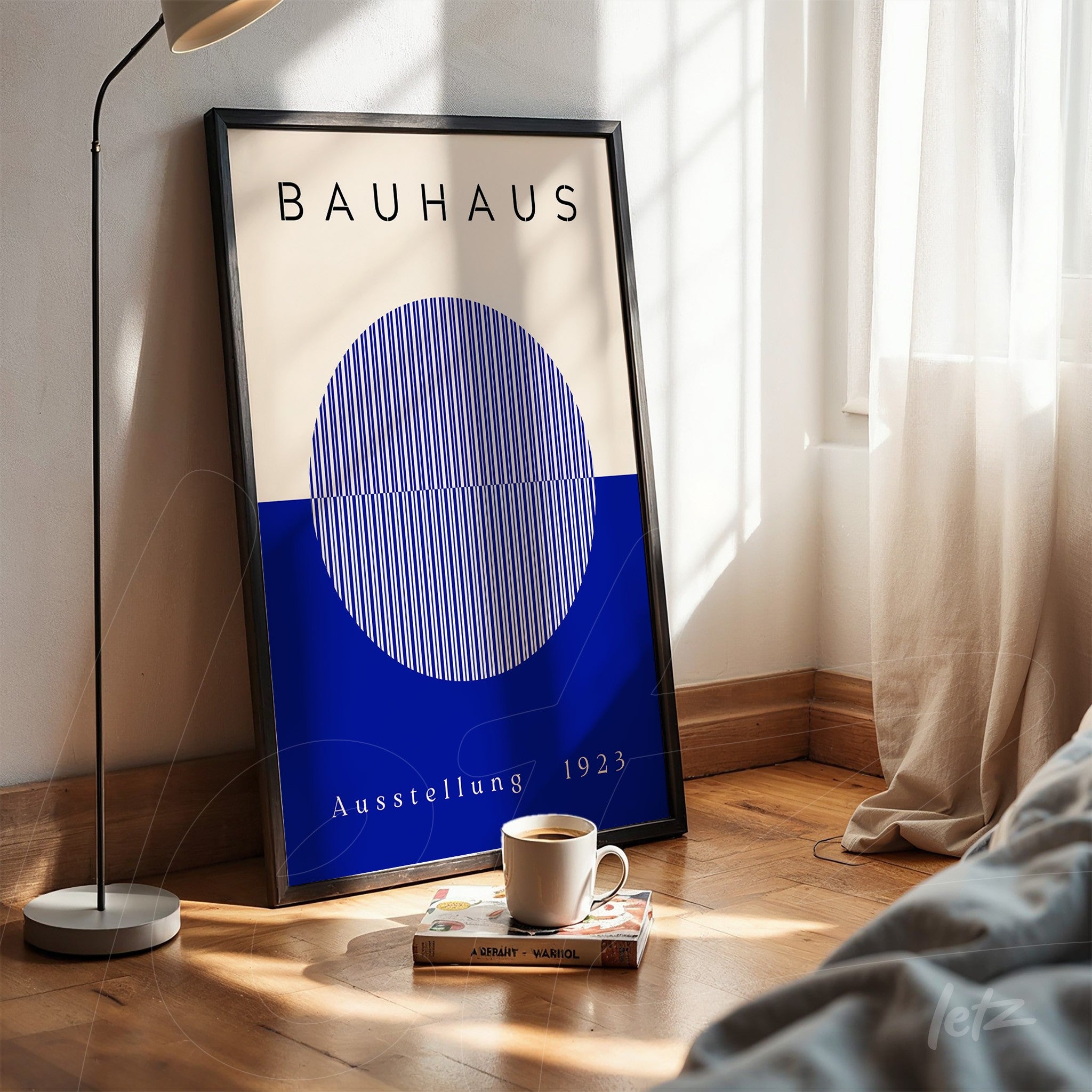 pôster impresso de design bauhaus com esfera azul e linhas brancas em moldura preta, apoiado no chão de madeira ao lado de xícara de café