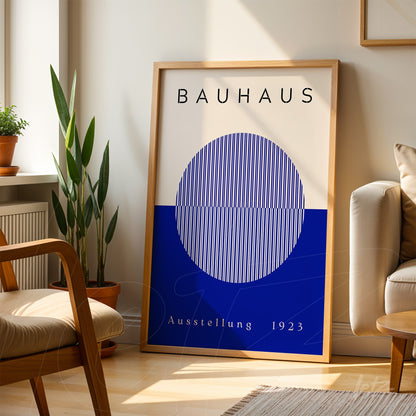 pôster impresso de arte bauhaus com círculo azul emoldurado em madeira clara, apoiado em piso de madeira junto a sofá creme