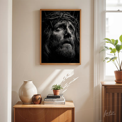 quadro em moldura de madeira clara com retrato em preto e branco de Cristo coroado de espinhos, exibido sobre uma mesa de madeira em ambiente iluminado