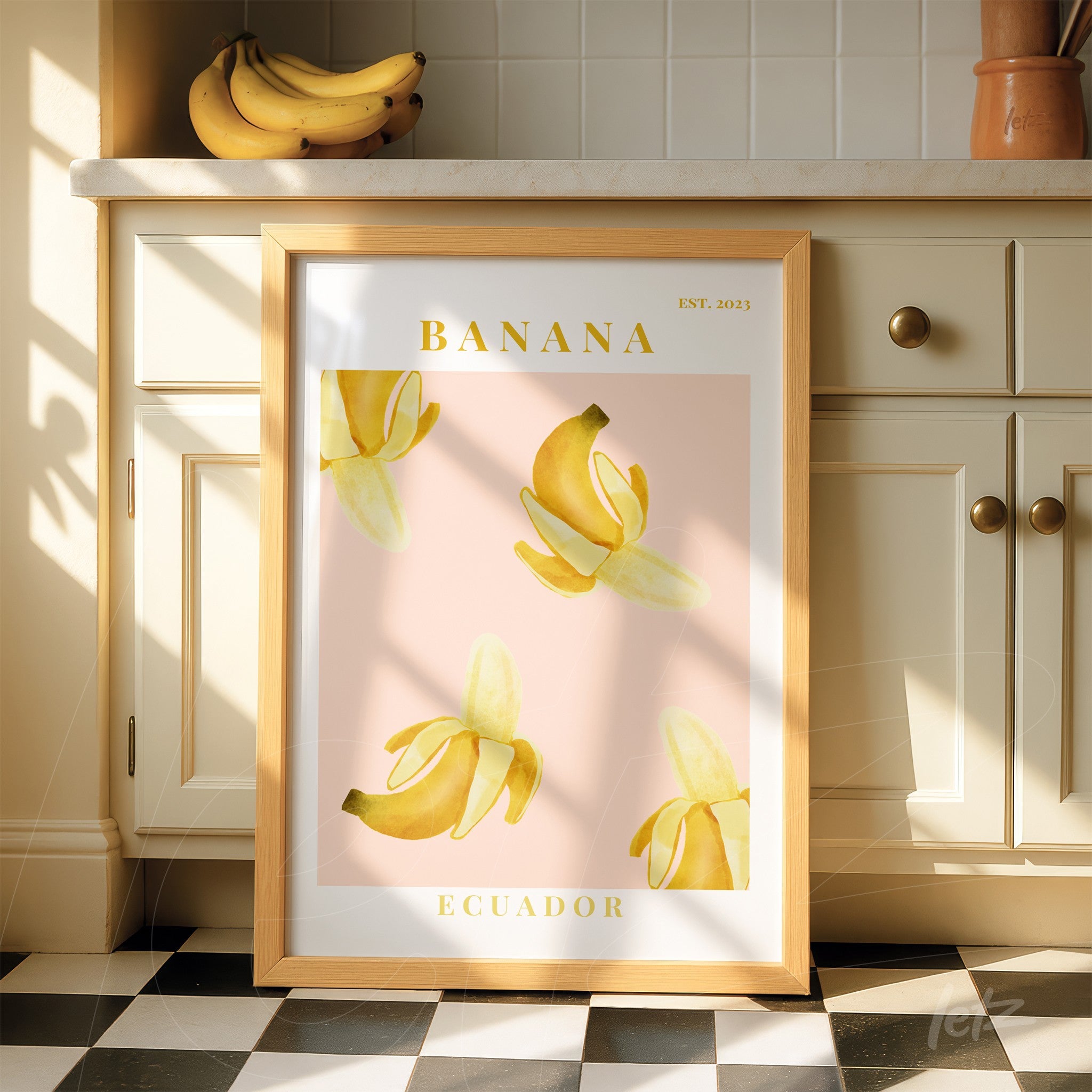 quadro emoldurado com temática de bananas em tons amarelos sobre fundo rosa claro, com moldura de madeira clara