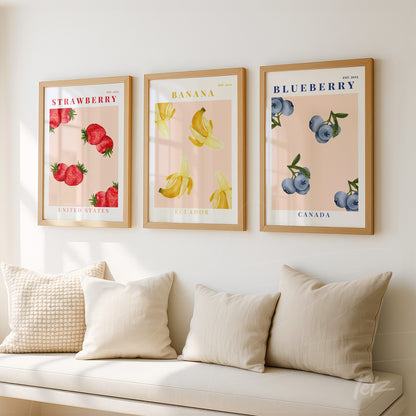 composição de três quadros em moldura de madeira clara, com ilustrações de frutas: morangos, bananas e mirtilos, sobre fundo suave
