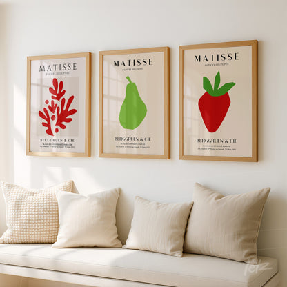 composição de três quadros decorativos com ilustrações em estilo moderno de um coral vermelho, uma pera verde e um morango vermelho, todos em molduras de madeira clara apresentando fundo neutro