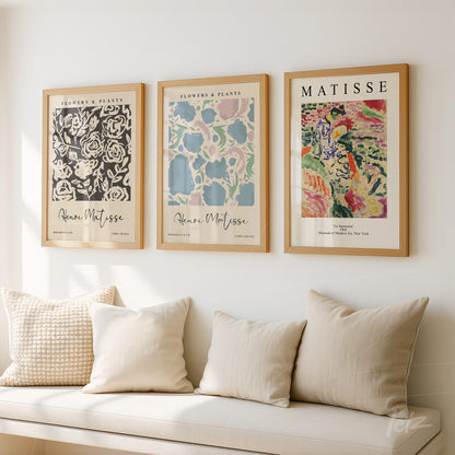composição com três quadros decorativos em moldura de madeira clara, exibidos sobre parede neutra, com ilustrações de flores e plantas no estilo de Henri Matisse