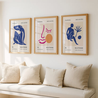 composição com três quadros de arte moderna em moldura de madeira clara, destacando formas abstratas em tons de azul, rosa e ocre sobre fundo neutro