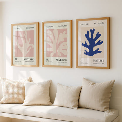 composição de três quadros com ilustrações em estilo moderno de folhas em tons pastéis e uma moldura clara, expostos sobre uma parede neutra com um sofá acolhedor ao primeiro plano