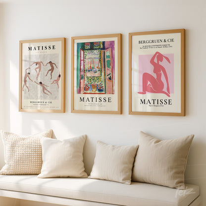 composição de três quadros decorativos com arte de Matisse, em moldura de madeira clara, sobre parede branca, com almofadas em sofá bege ao fundo