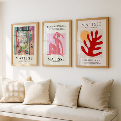 composição de três quadros com obras de Matisse em moldura de madeira clara, exibidos sobre uma parede branca, com almofadas em sofá cream ao fundo