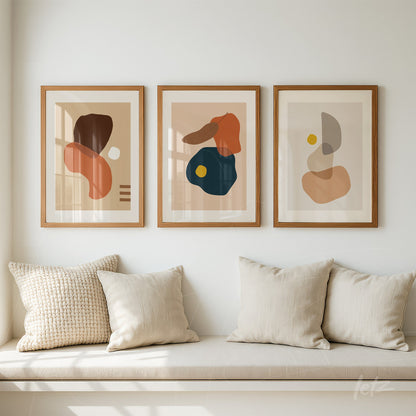 três quadros com arte abstrata de formas orgânicas coloridas em molduras de madeira sobre parede clara