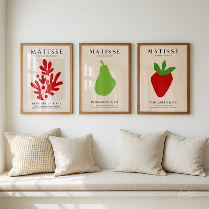composição de três quadros com arte simples de frutas e vegetação em molduras de madeira clara, exibidos sobre sofá neutro