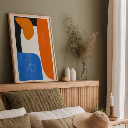 quadro com arte abstrata em tons de azul e laranja em moldura de madeira clara, apoiado sobre cabeceira de cama com travesseiros em tons terrosos