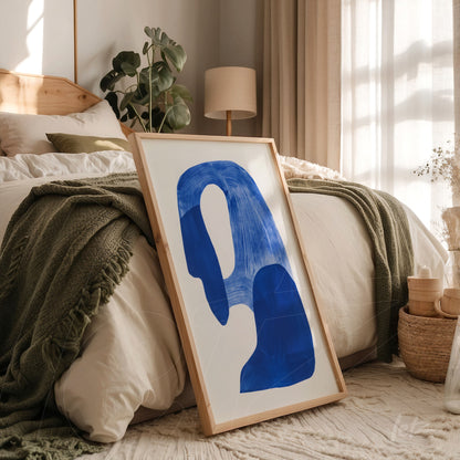 quadro com arte abstrata em azul e branco em moldura de madeira clara, apoiado na cama com colcha verde