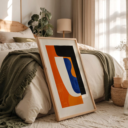 quadro com arte abstrata em tons de laranja, azul e preto com moldura de madeira clara apoiado em cama com edredom branco e manta verde