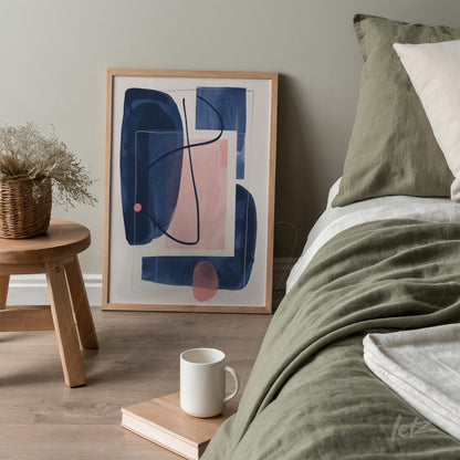 quadro com arte abstrata em tons de azul e rosa em moldura clara, exibido próximo a uma cama com roupa de cama verde