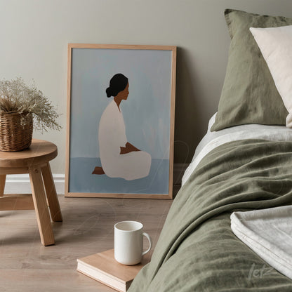 quadro com arte minimalista retratando uma mulher sentada em tons neutros, em moldura de madeira clara, apoiado ao lado de uma cama com roupa de cama verde
