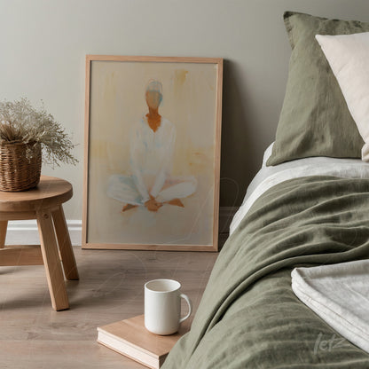 quadro em moldura de madeira clara com arte abstrata de figura humana em tons suaves, apoiado ao lado de um colchão com lençóis em verde e almofadas claras