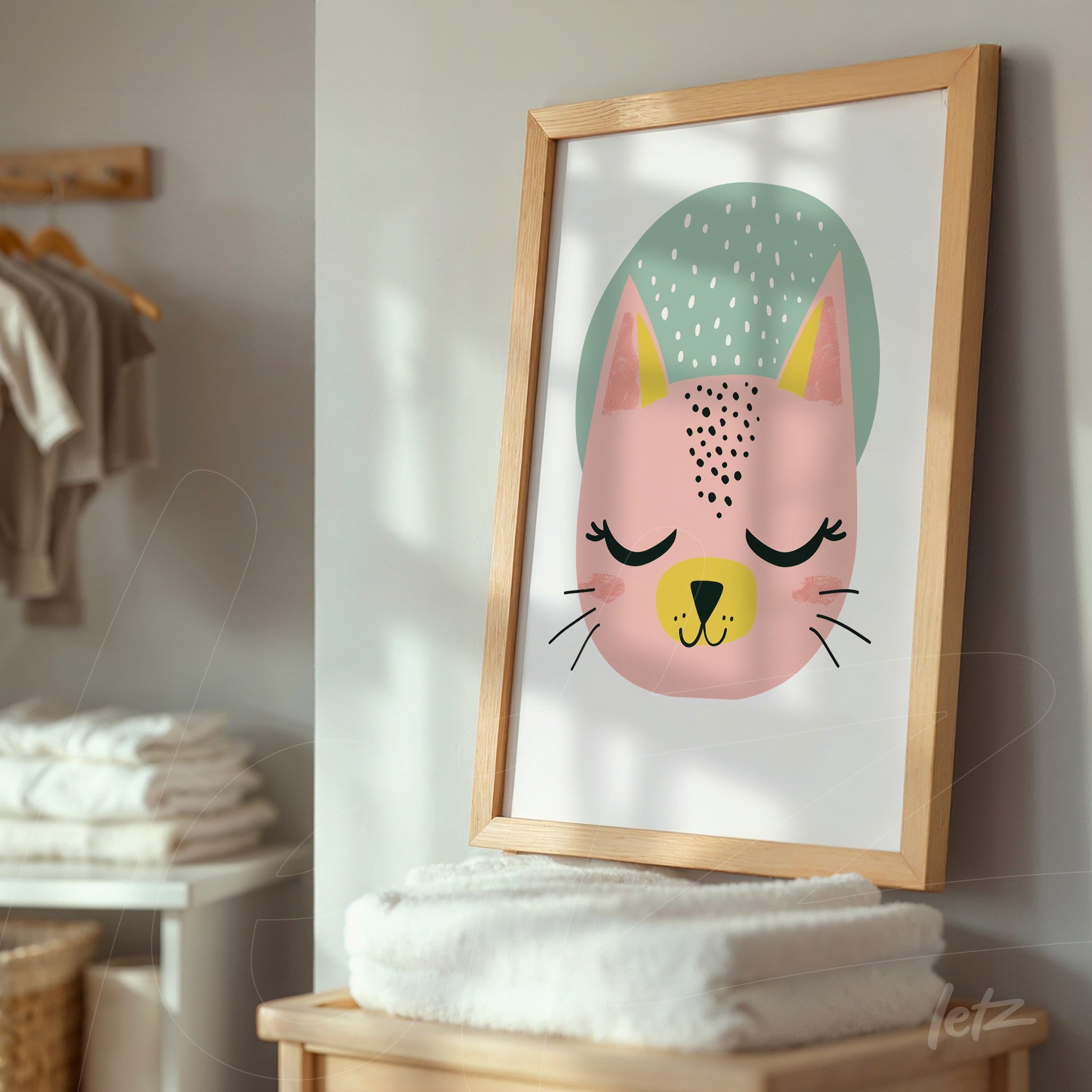 quadro com ilustração de gato estilizado em moldura de madeira clara, exposto em ambiente com toalhas empilhadas